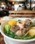 A steaming bowl of Filipino Beef Bulalo with bone marrow, corn, bok choy, green beans, and potatoes.